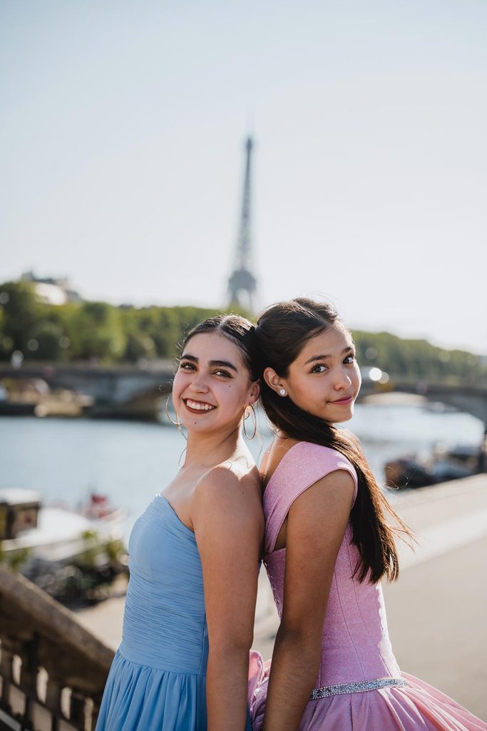 Dos jóvenes con vestidos pastel azul y rosa sonriendo junto al Sena con la Torre Eiffel de fondo / Two young women in pastel blue and pink dresses smiling by the Seine with the Eiffel Tower behind