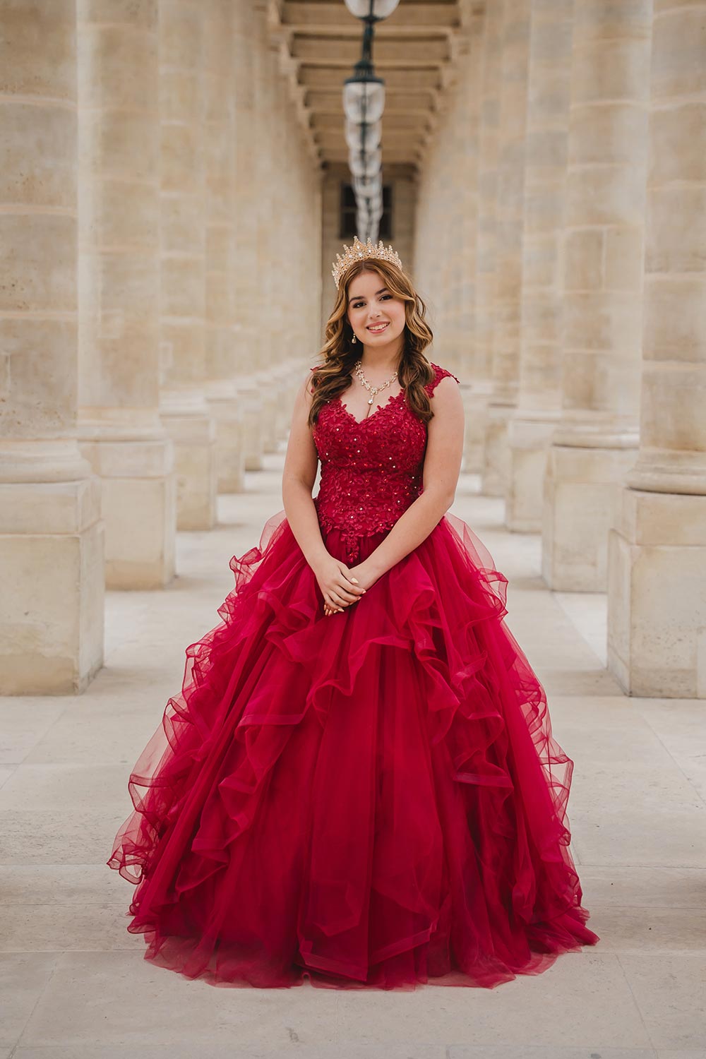 Quinceañera con vestido rojo de tul con volados y corona posando en la columnata del Palais Royal en París / Quinceañera in a ruffled red tulle gown and crown posing in the Palais Royal colonnade in Paris