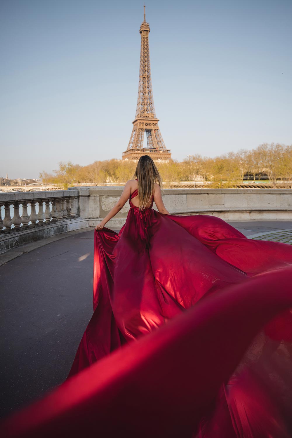 Quinceañera de espaldas con vestido rojo flotando al viento frente a la Torre Eiffel desde un puente en París / Quinceañera from behind with a red gown flowing in the wind facing the Eiffel Tower from a Paris bridge