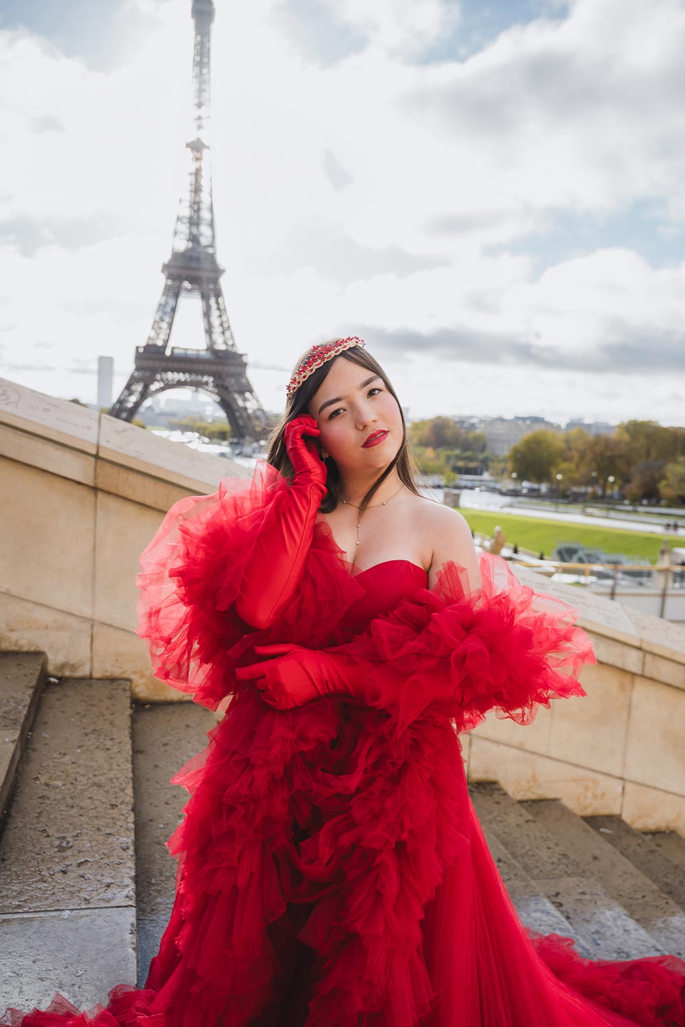 Quinceañera con vestido rojo de tul en capas, guantes largos y corona en las escaleras del Trocadéro frente a la Torre Eiffel / Quinceañera in a layered red tulle gown, long gloves, and a crown on the Trocadéro steps in front of the Eiffel Tower