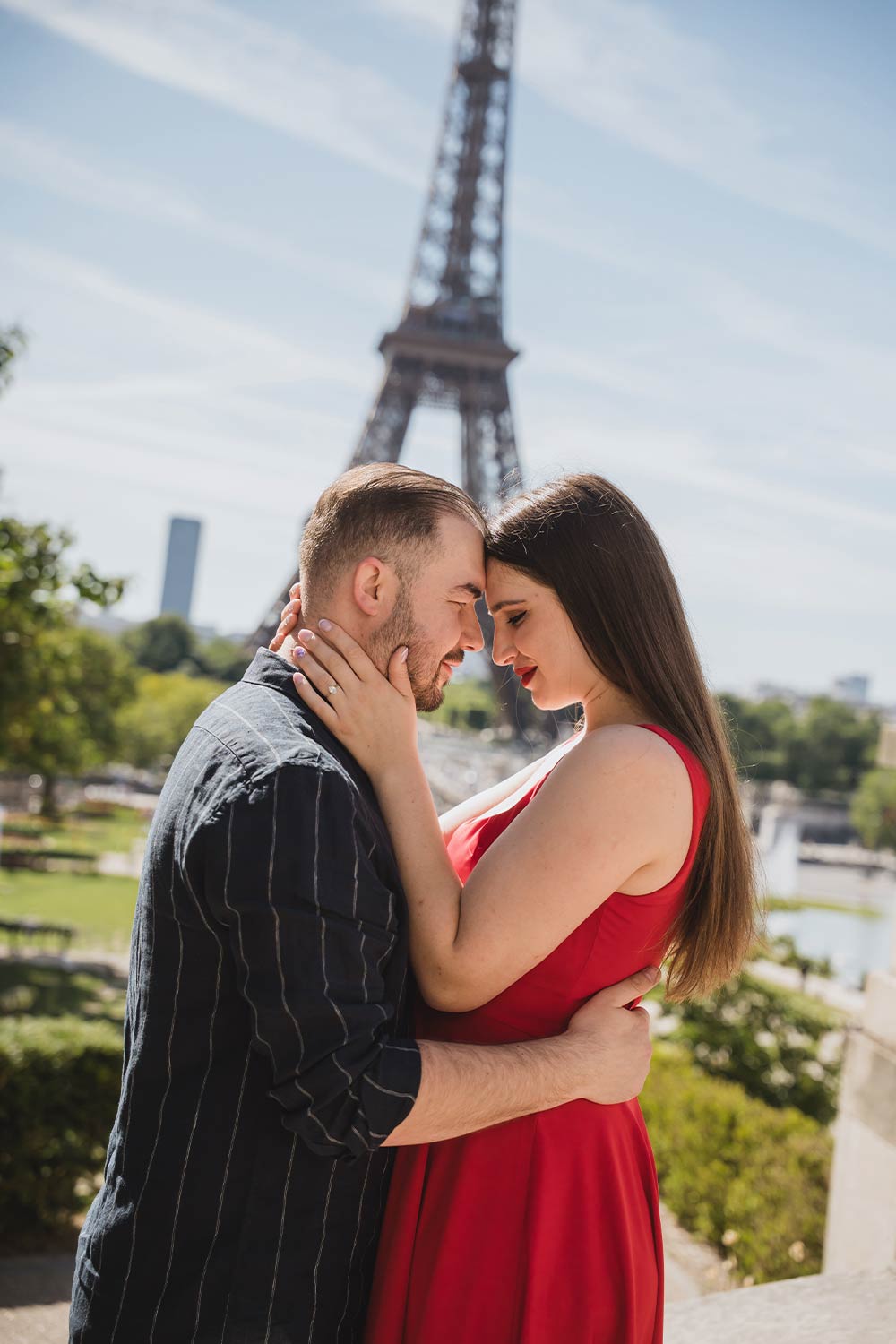 Pareja abrazada frente a frente con la Torre Eiffel de fondo, ella con vestido rojo, en el Trocadéro de París / Couple embracing face to face with the Eiffel Tower behind, her in a red dress, at the Trocadéro in Paris