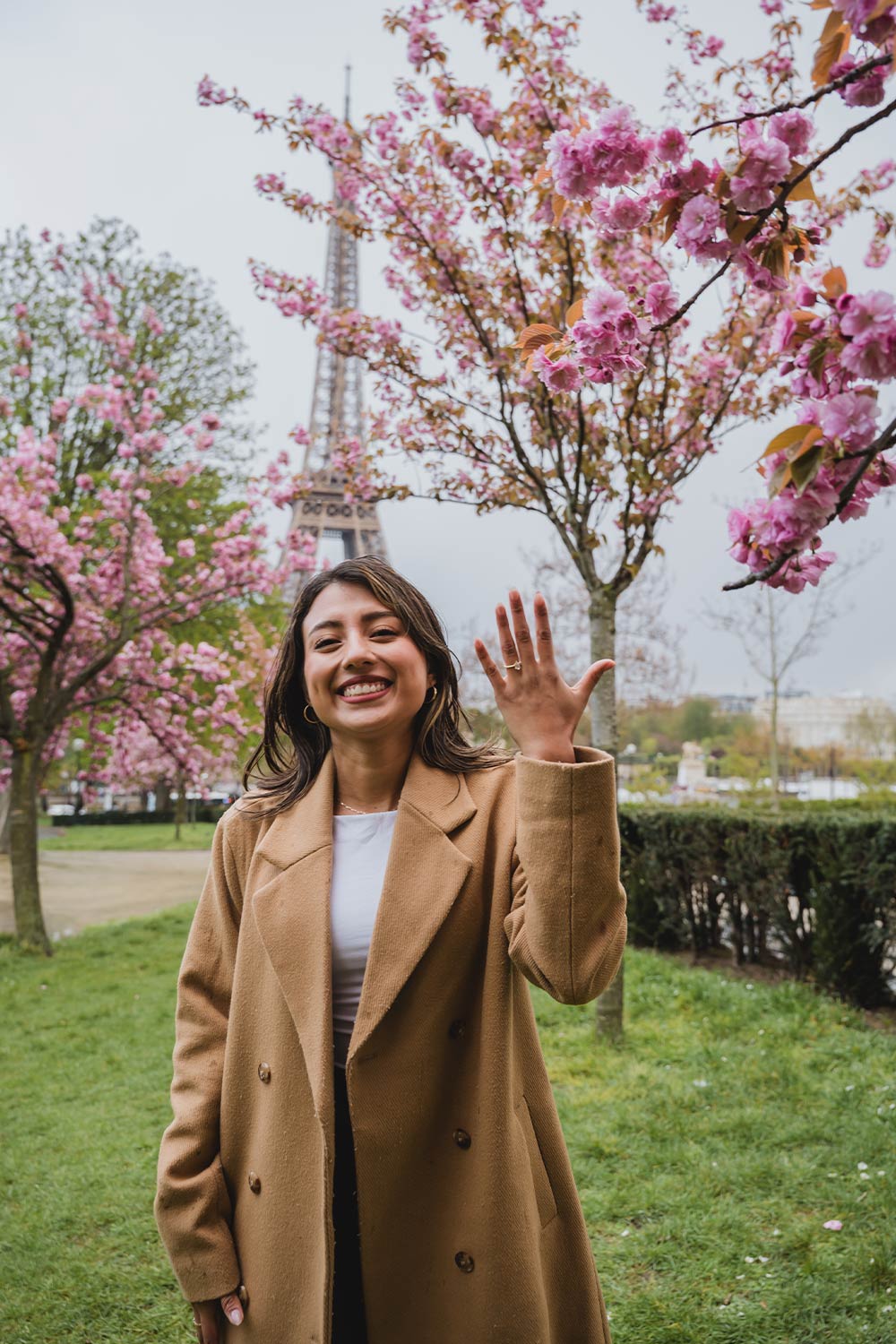 Mujer sonriendo y mostrando su anillo de compromiso bajo cerezos en flor con la Torre Eiffel de fondo en París / Woman smiling and showing off her engagement ring beneath cherry blossoms with the Eiffel Tower behind, Paris